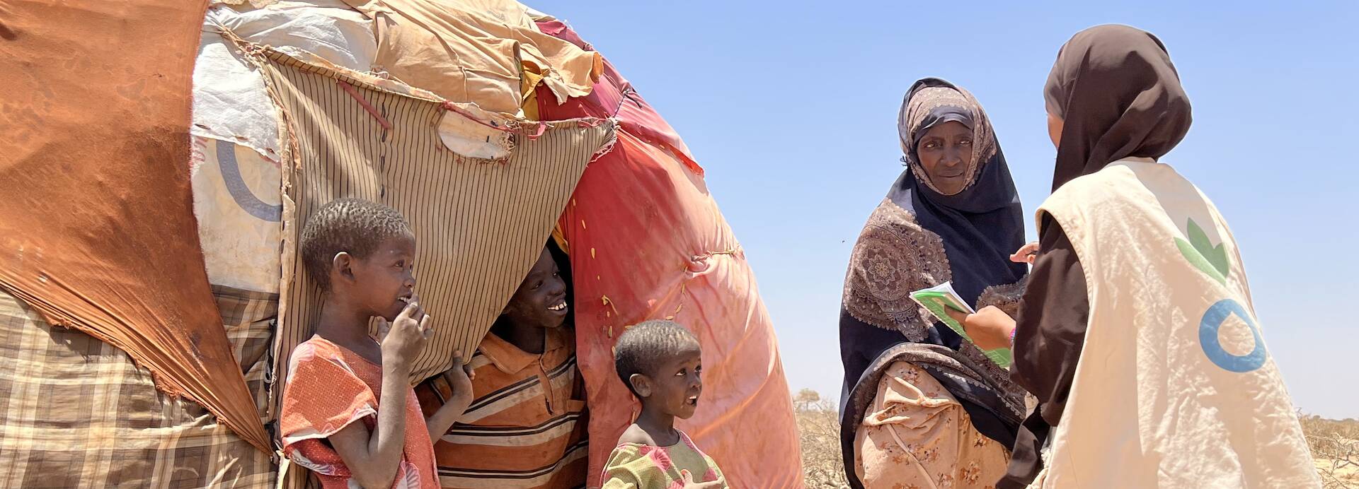 Mitarbeitende von Aktion gegen den Hunger sprechen mit einer Mutter und ihren Kindern vor ihrem Zelt in Somalia.