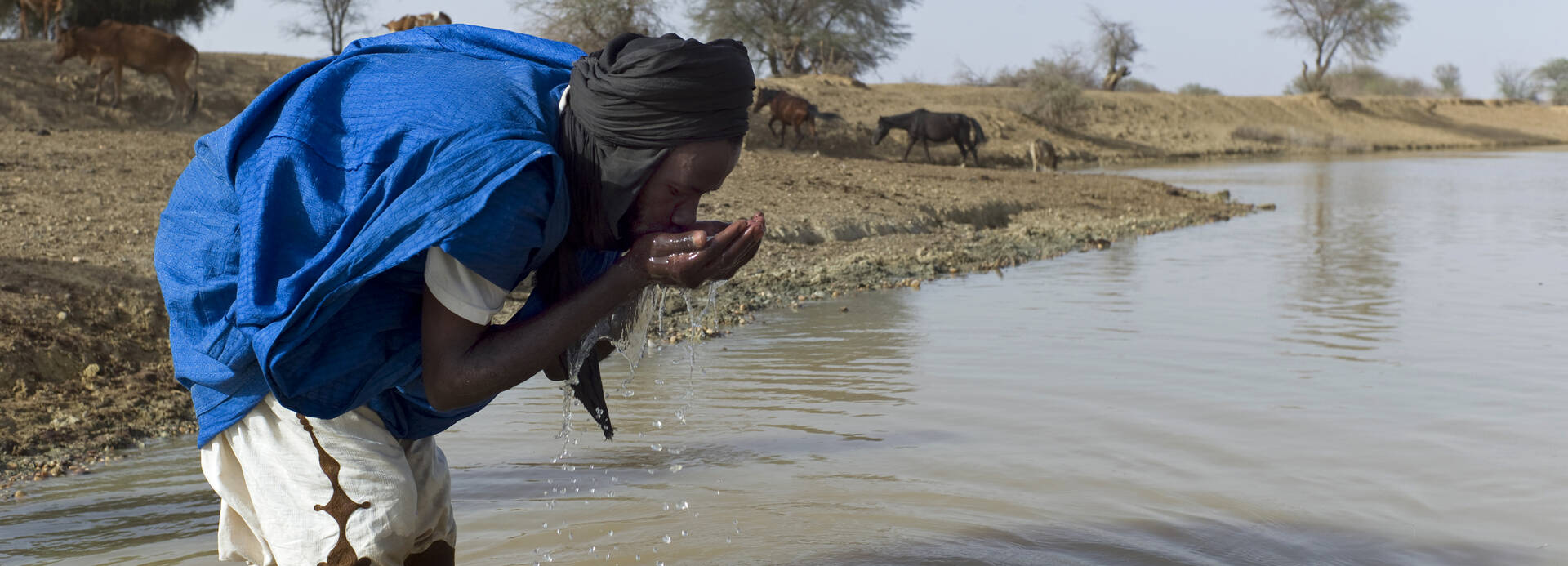 Seewasser trinken kann schnell gefährlich werden – doch vielen Menschen bleibt nichts anderes übrig. Ein Mann steht in einem verschmutzten See und trinkt Seewasser