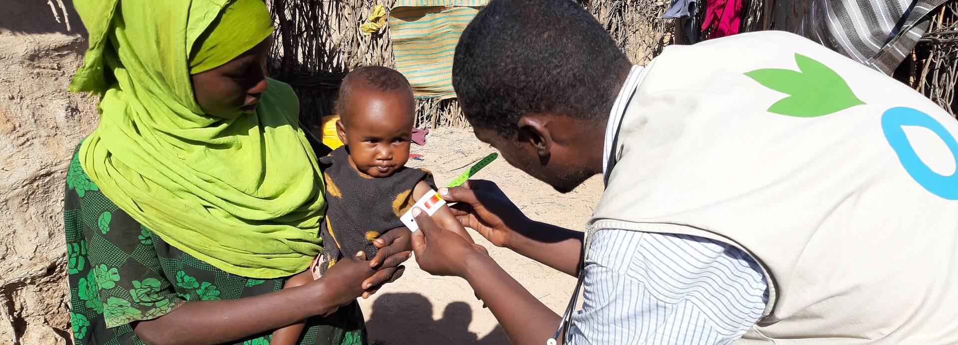 Ein Mitarbeiter von Aktion gegen den Hunger untersucht ein Kleinkind in den Armen der Mutter auf Mangelernährung.