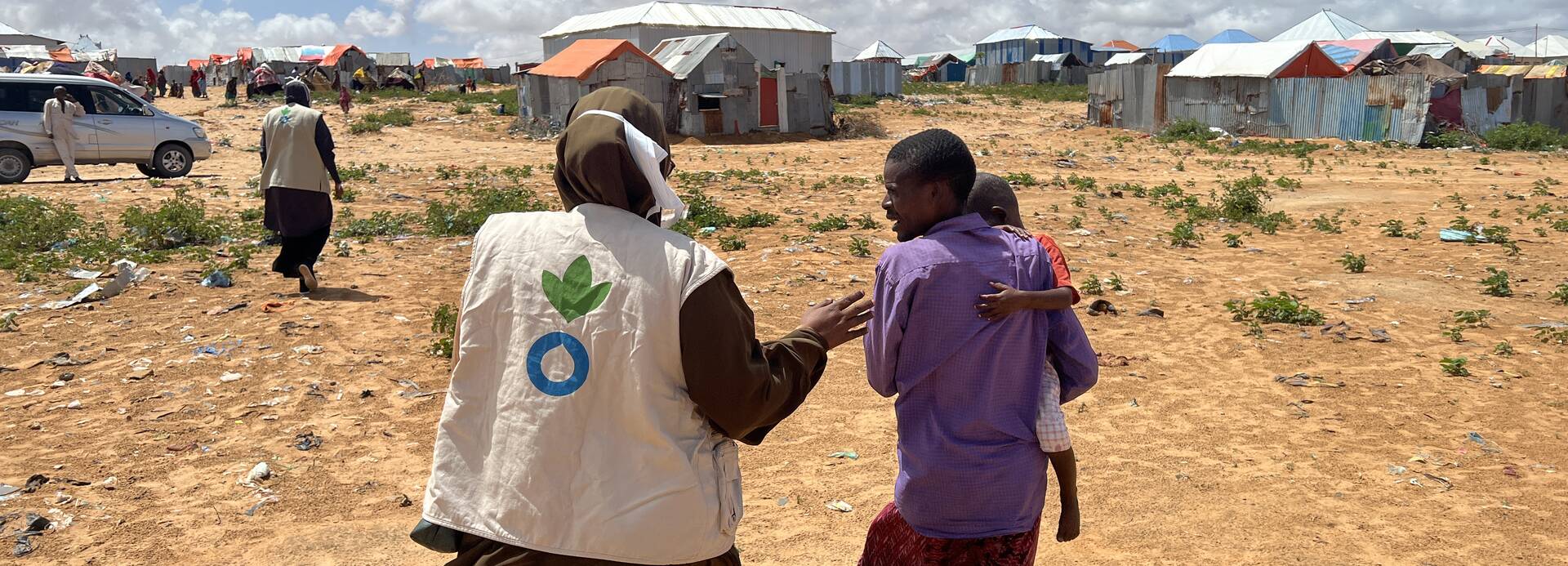 Eine Mitarbeiterin von Aktion gegen den Hunger in Somalia begleitet einen Vater mit Kind auf dem Arm durch ein Camp.