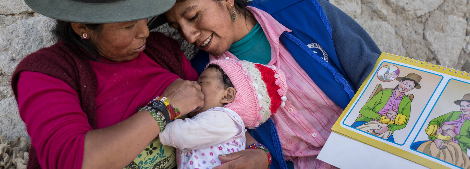 Zwei Frauen aus Peru stillen ein kleines Mädchen nach einer bildlichen Anleitung.