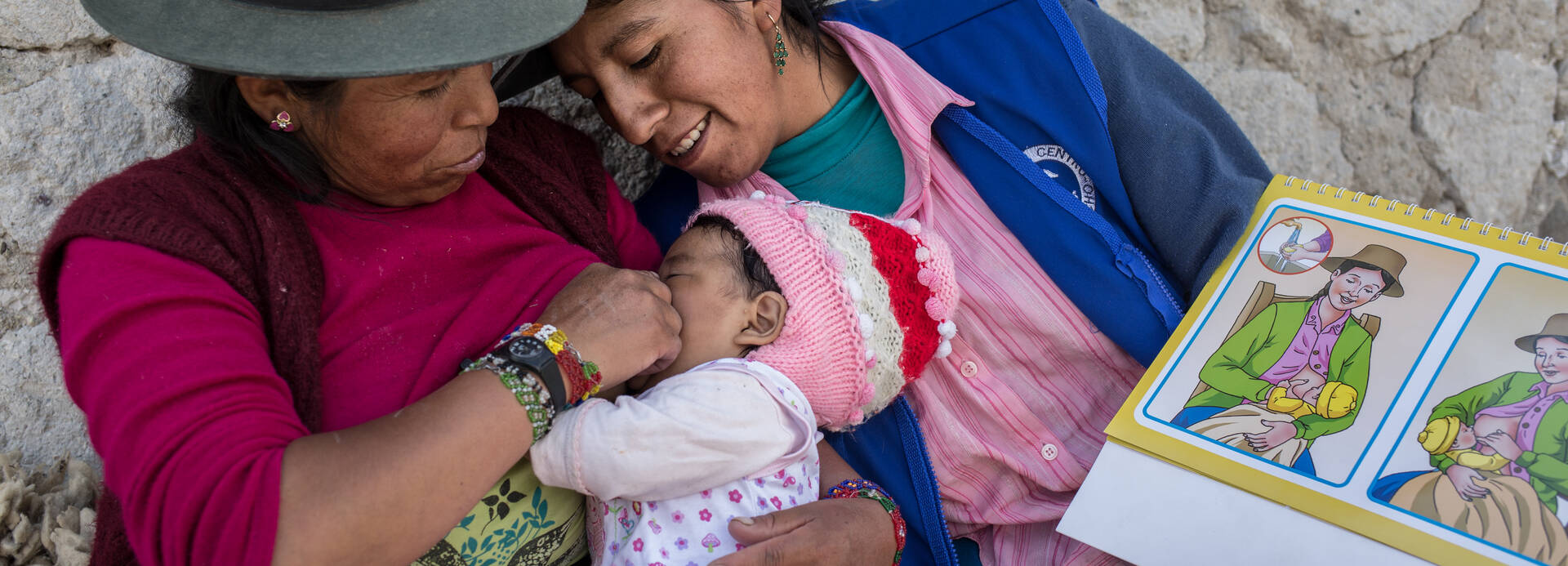 Stillberaterinnen in Peru unterstützen Mütter dabei, das Stillen zu lernen. Zwei Frauen aus Peru stillen ein kleines Mädchen nach einer bildlichen Anleitung.