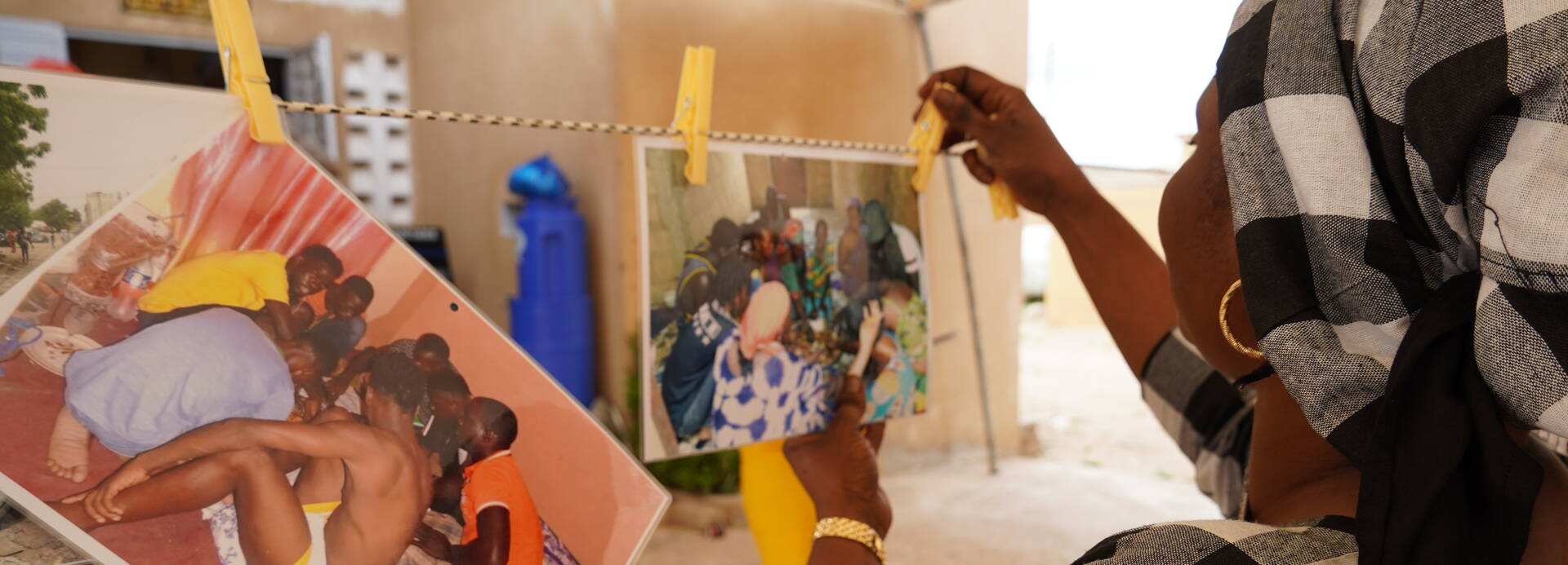 Fotoprojekt im Senegal: Eine Teilnehmende hängt Fotos auf Eine Frau aus dem Senegal hängt selbstgeschossene Fotos auf einer Leine auf