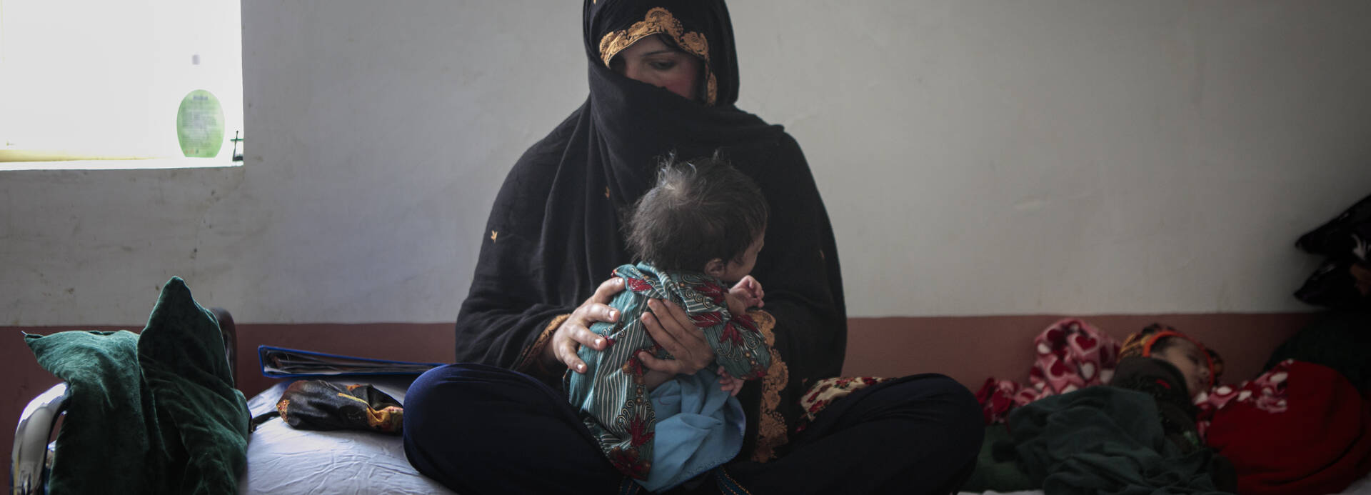 Eine Mutter sitzt mit ihren mangelernährten Zwillingen auf einem Bett in einem unserer Krankenhäuser in Afghanistan.