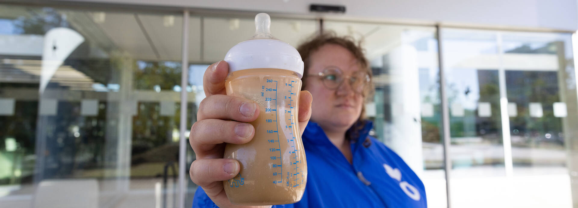 Nicht steril und korrekt angerührte Babymilch bringt jährlich hunderttausende Babys in Gefahr. Aktion-gegen-den-Hunger-Mitarbeiterin Kira hält eine Flasche mit verschmutzter Babymilch vor der Nestlé-Zentrale in Frankfurt am Main in die Kamera