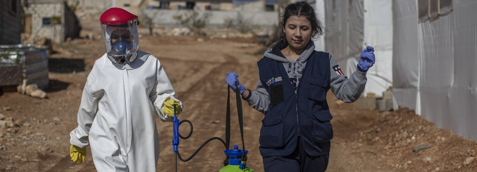 Im Libanon ist 2022 Cholera ausgebrochen. Unsere Mitarbeitenden unterstützen bei der Desinfektion. Zwei MItarbeitende von Aktion gegen den Hunger tragen Desinfektionsmittel durch ein Dorf im Libanon, um Cholera-Bakterien zu beseitigen.
