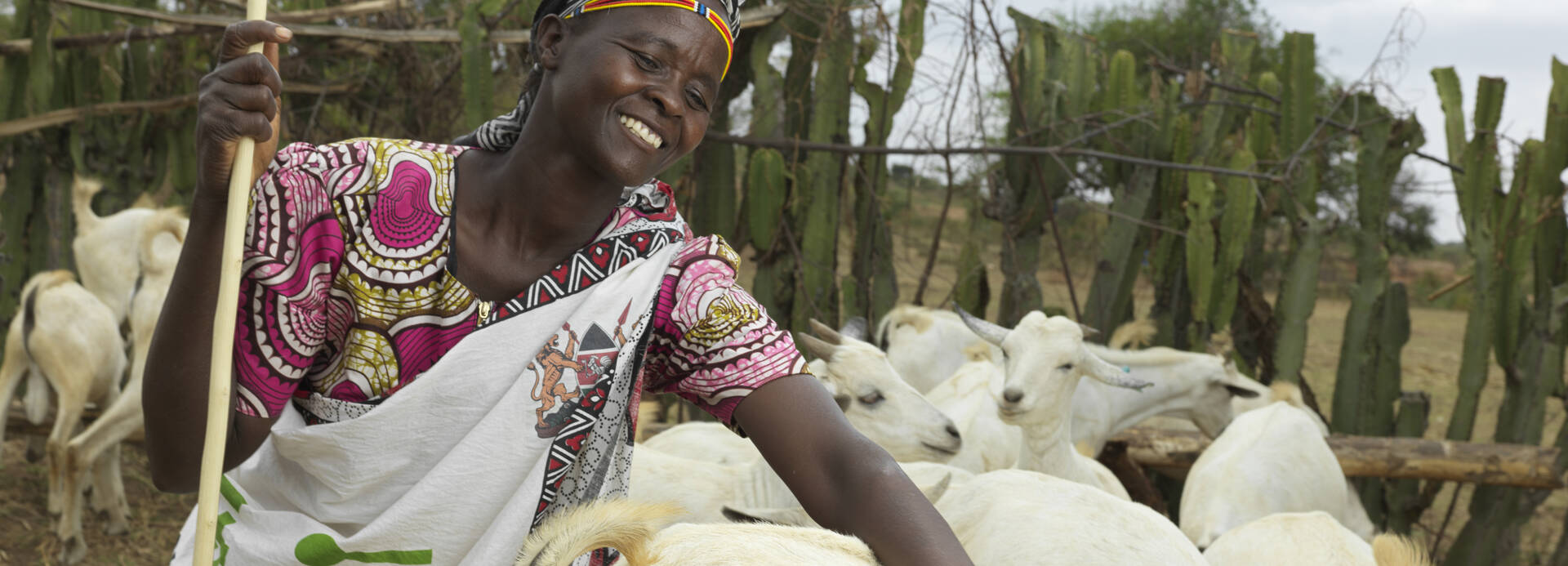 Rosalyne steht lachend im Ziegengehege in Kenia und streichelt eine Ziege.