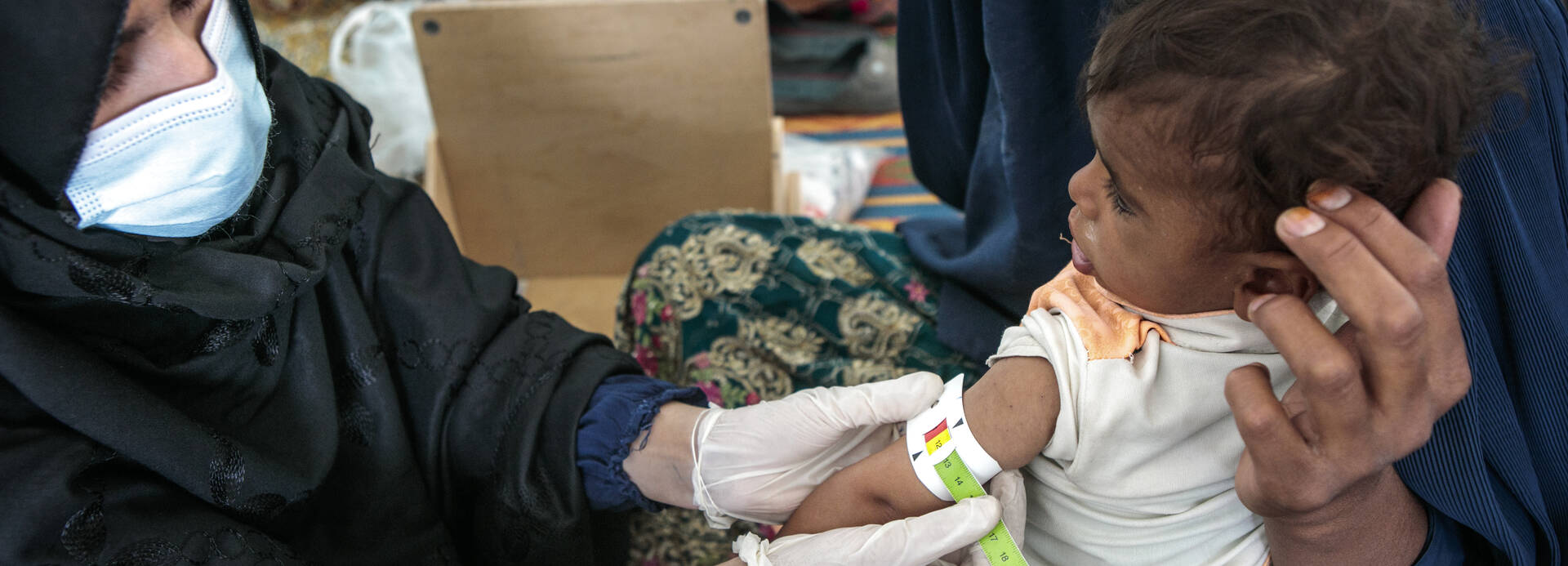Eine Gesundheitsmitarbeiterin von Aktion gegen den Hunger misst einem Kind in den Armen der Mutter mit einem MUAC-Band den Armumfang.