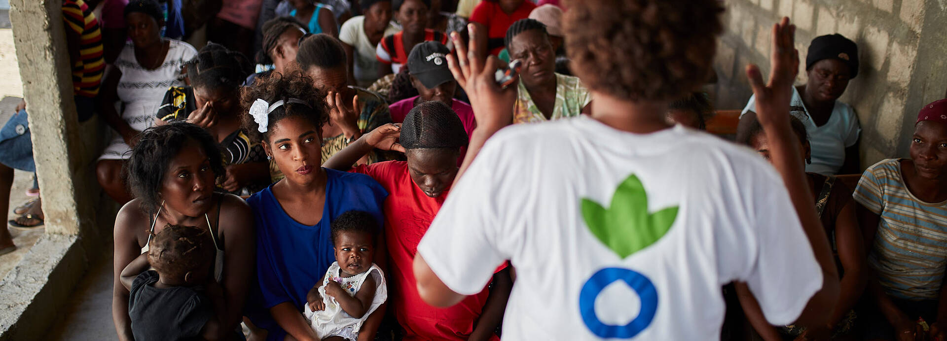 Eine Mitarbeiterin von Aktion gegen den Hunger erklärt einer Gruppe Frauen, Männer und Kinder aus Haiti, wie sie sich mit gesunder Ernährung und Hygiene vor Cholera schützen können.