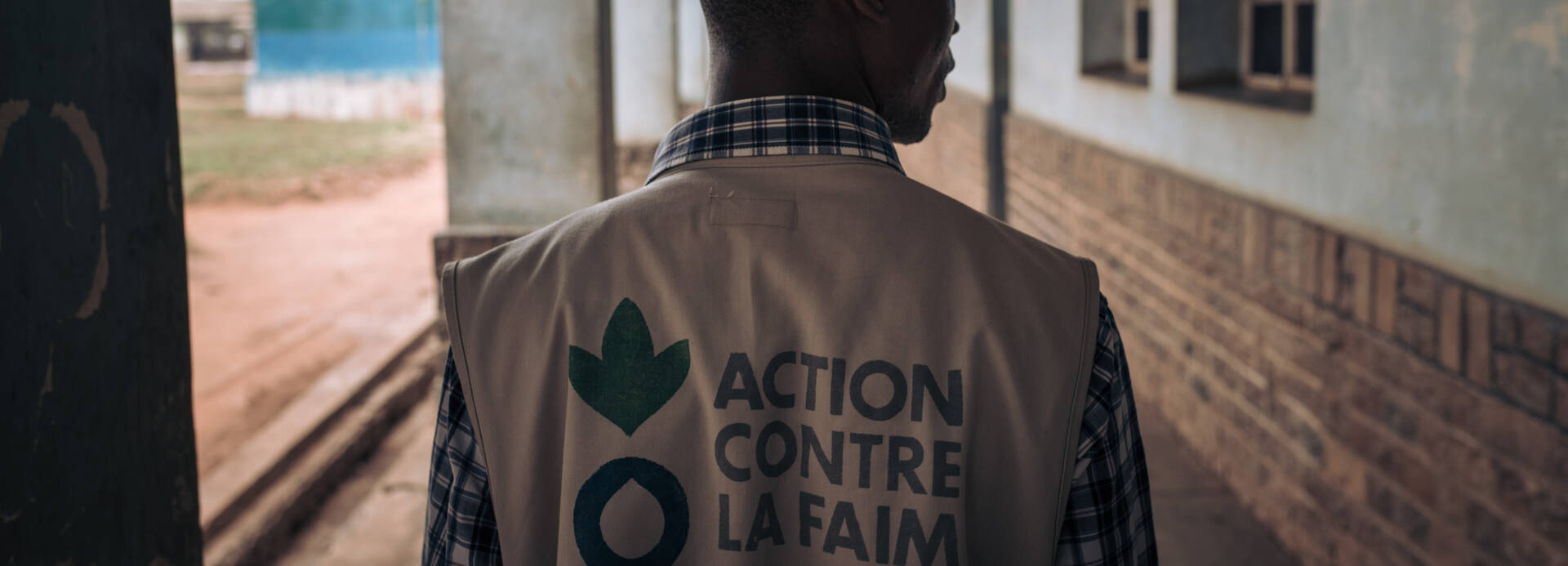 Ein Mitarbeiter von Aktion gegen den Hunger von hinten in einem Gang in der Demokratischen Republik Kongo, auf seiner Weste das Logo