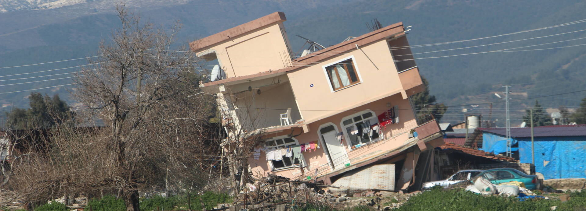 Ein Haus ist nach dem Erdbeben in der Region Hatay zur Seite gekippt, im Hintergrund Berge.