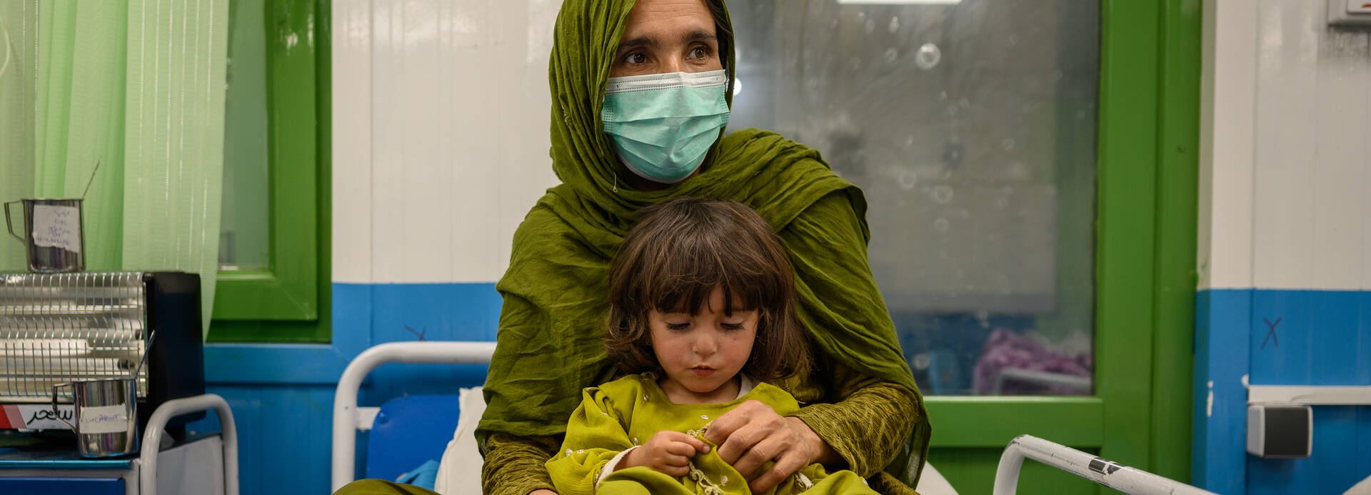 Eine afghanische Mutter sitzt zusammen mit ihrer Tochter auf einem Bett in unserer Ernährungsstation in einer Klinik in Kabul.