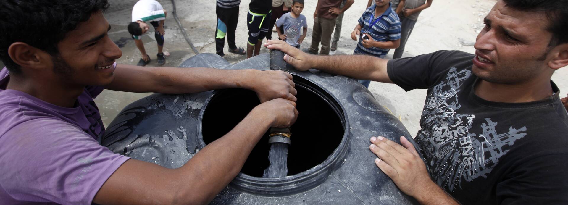 Während der Kämpfe mussten alle WASH-Aktivitäten ausgesetzt werden – es ist wichtig, diese nun in der Waffenruhe und darüber hinaus fortführen zu können, etwa um genügend Wasser bereitzustellen. Zwei Männer füllen einen Wassertank mit frischem Wasser, im Hintergrund stehen weitere Menschen