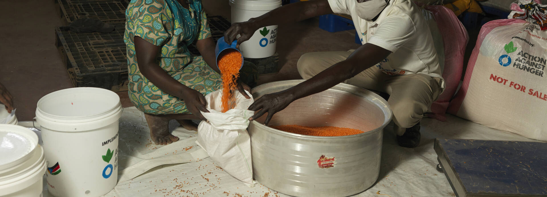Ein Mitarbeiter von Aktion gegen den Hunger füllt Getreide in einen Sack einer Frau aus dem Südsudan.