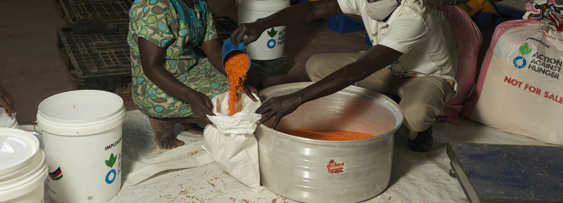 Humanitäre Hilfe wie die Unterstützung mit Lebensmitteln wäre mit gekürztem Etat weltweit eingeschränkt. Millionen Menschen würden darunter leiden. Ein Mitarbeiter von Aktion gegen den Hunger füllt Getreide in einen Sack einer Frau aus dem Südsudan.