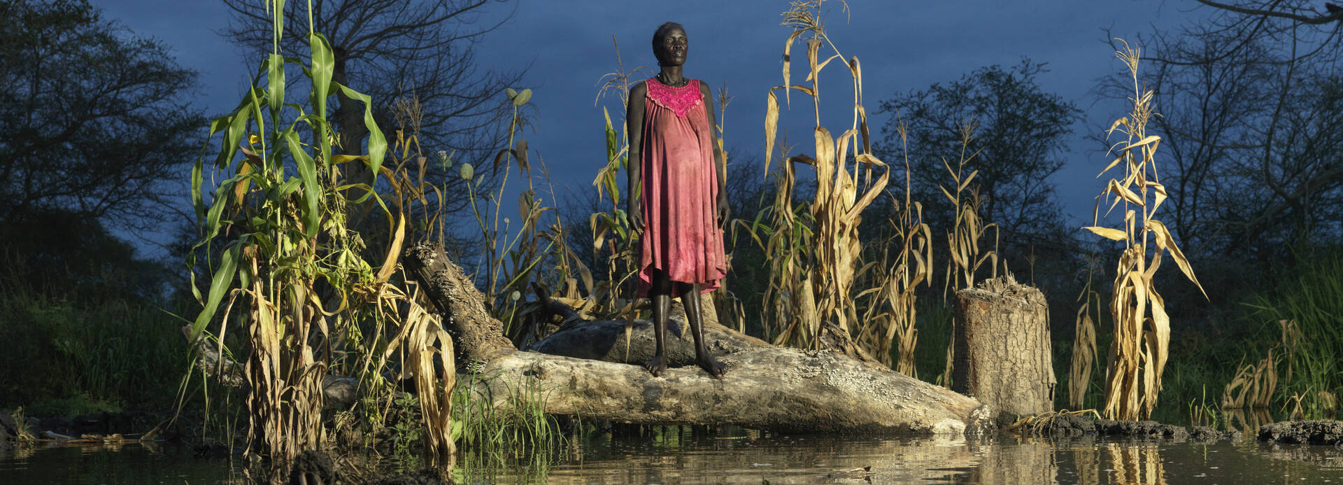 Eine Frau im roten Kleid steht neben ihrem überfluteten Maisfeld. Starke Überschwemmungen im Südsudan haben Felder, Häuser und Straßen zerstört.