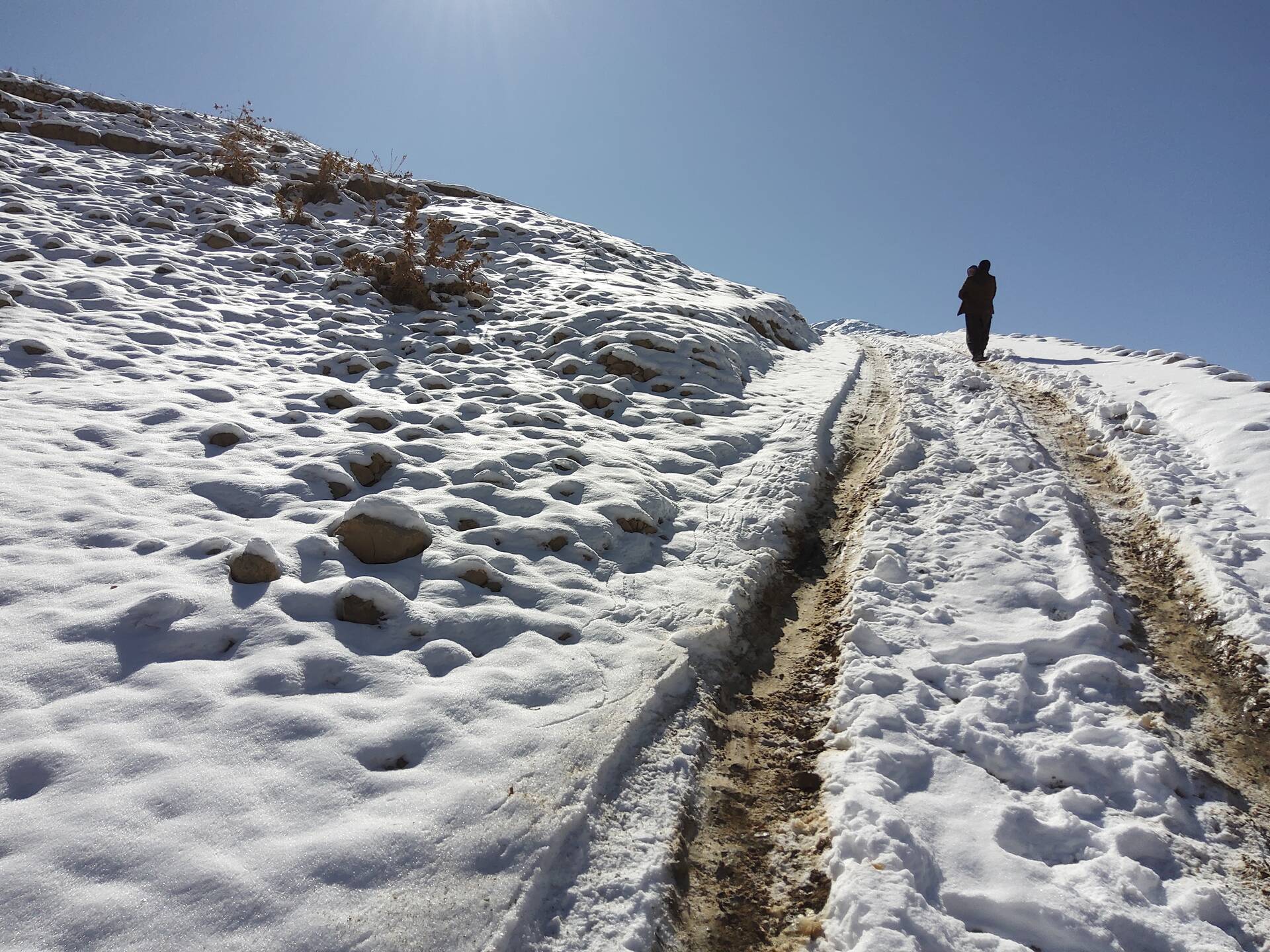 Ein Vater trägt sein Kind über einen verschneiten Weg im winterlichen Afghanistan zu einem abgelegenen Krankenhaus. Die beiden sind nur von hinten zu sehen. Ein Vater trägt sein Kind über einen verschneiten Weg im winterlichen Afghanistan zu einem abgelegenen Krankenhaus. Die beiden sind nur von hinten zu sehen.