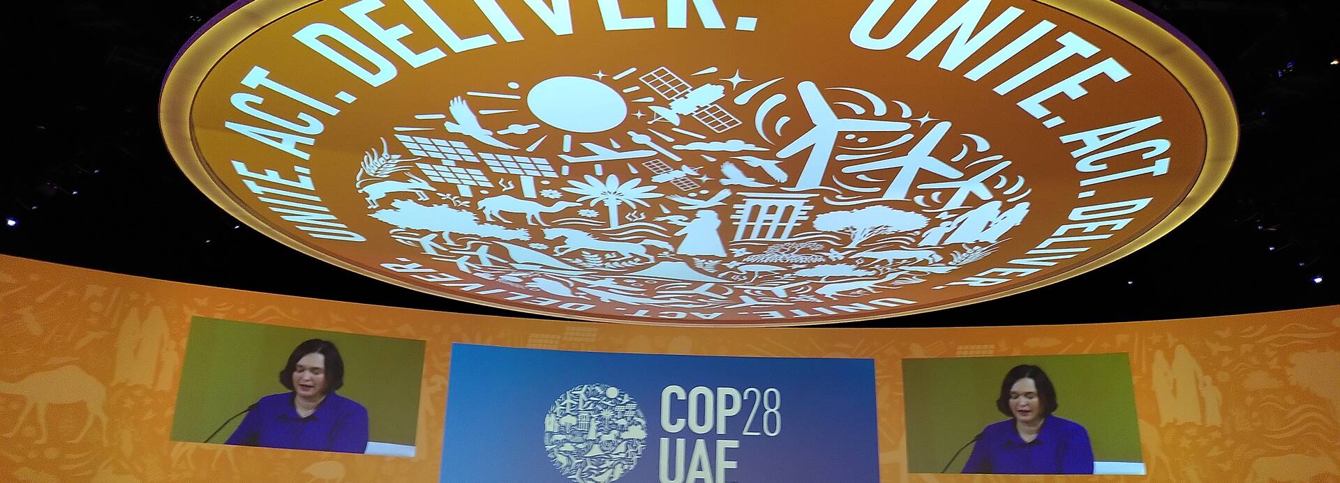 Im Plenarsaal der Klimakonferenz in Dubai sitzen die Vertreter*innen der Staaten und hören der Sprecherin vorne zu. Über allen wölbt sich eine große Kuppel mit der Aufschrift "Unite, Act, Deliver". Im Plenarsaal der Klimakonferenz in Dubai sitzen die Vertreter*innen der Staaten und hören der Sprecherin vorne zu. Über allen wölbt sich eine große Kuppel mit der Aufschrift "Unite, Act, Deliver".