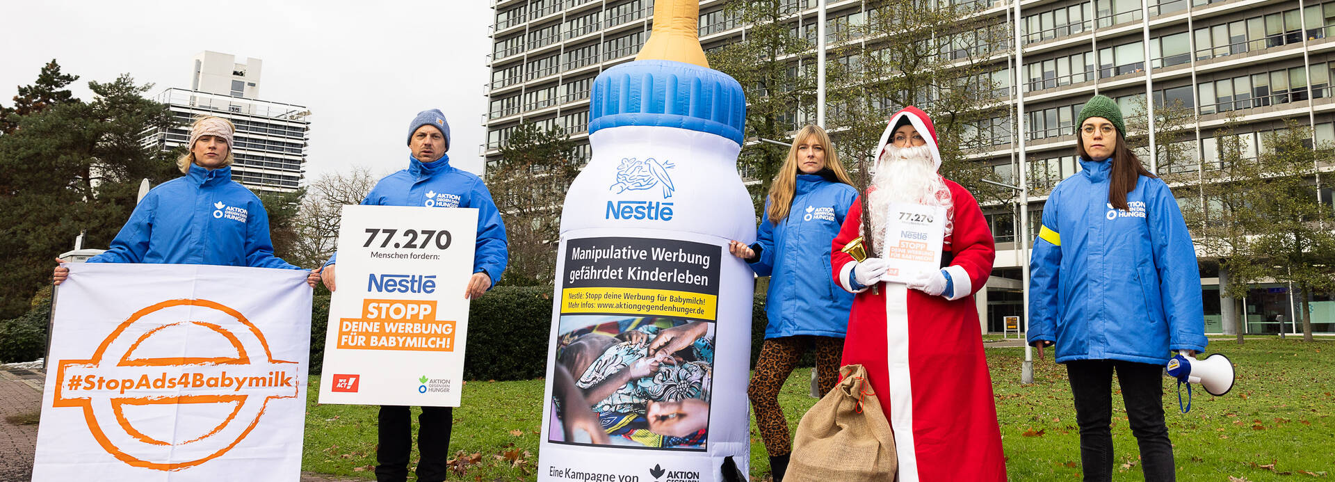 Das Team von Aktion gegen den Hunger und der Nikolaus stehen zusammen mit einer aufblasbaren Babymilchflasche vor der Nestlé-Zentrale in Frankfurt am Main.