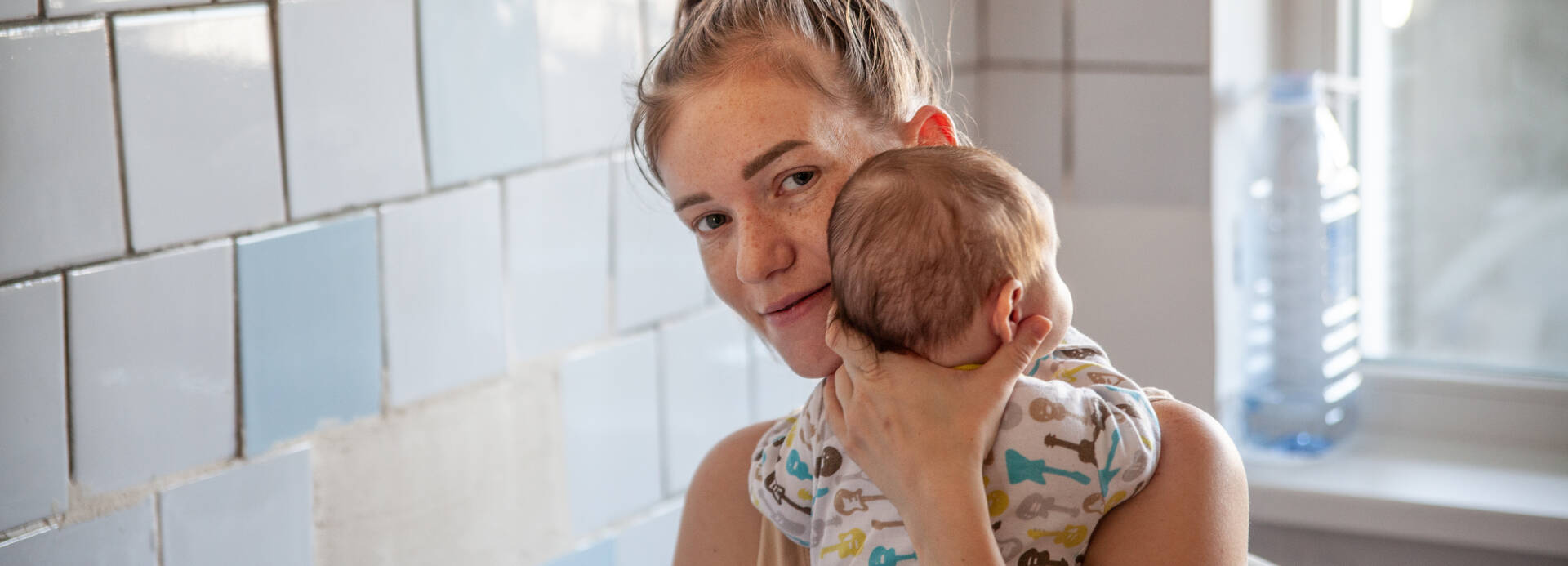 Eine junge Mutter in einem Kinderkrankenhaus in Moldau hält ihr Neugeborenes schützend im Arm und lächelt in die Kamera.