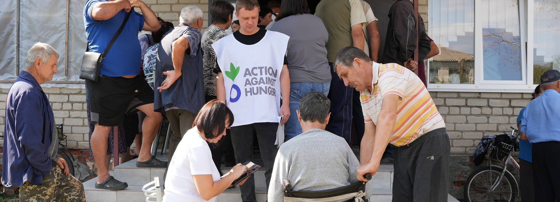 Mitarbeitende von Aktion gegen den Hunger unterstützen ältere Menschen in der Ukraine vor einem Haus.