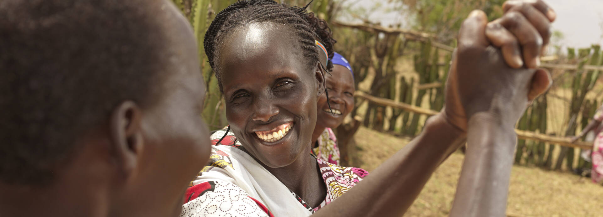 Frauen aus Kenia schlagen freudig ein, eine strahlt dabei in die Kamera.