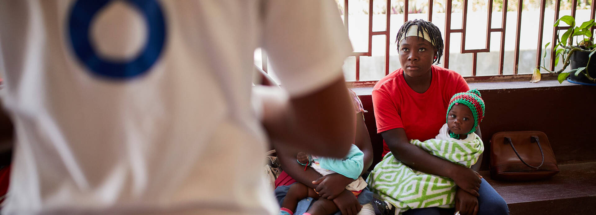 Eine Frau sitzt auf einer Bank mit einem Kind im Arm, während sie einer Erklärung eines unserer Mitarbeiterin in Haiti zuhört.