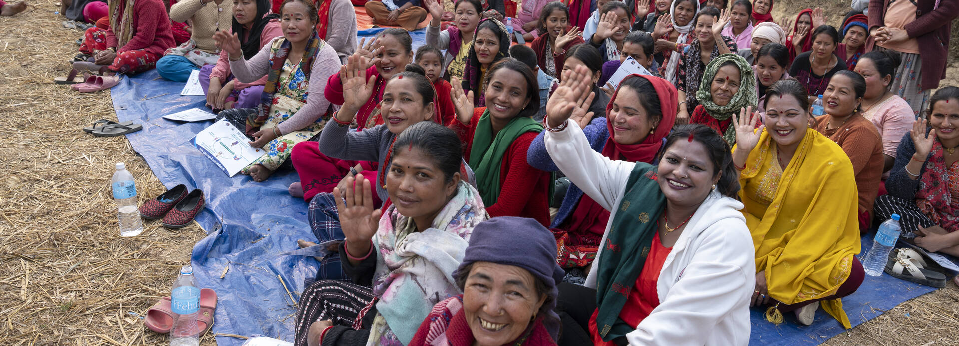 Goma und die anderen Frauen aus ihrem Dorf in Nepal sitzen nach einer Demonstration für Ernährungssicherheit gemeinsam auf dem Boden und winken in die Kamera.