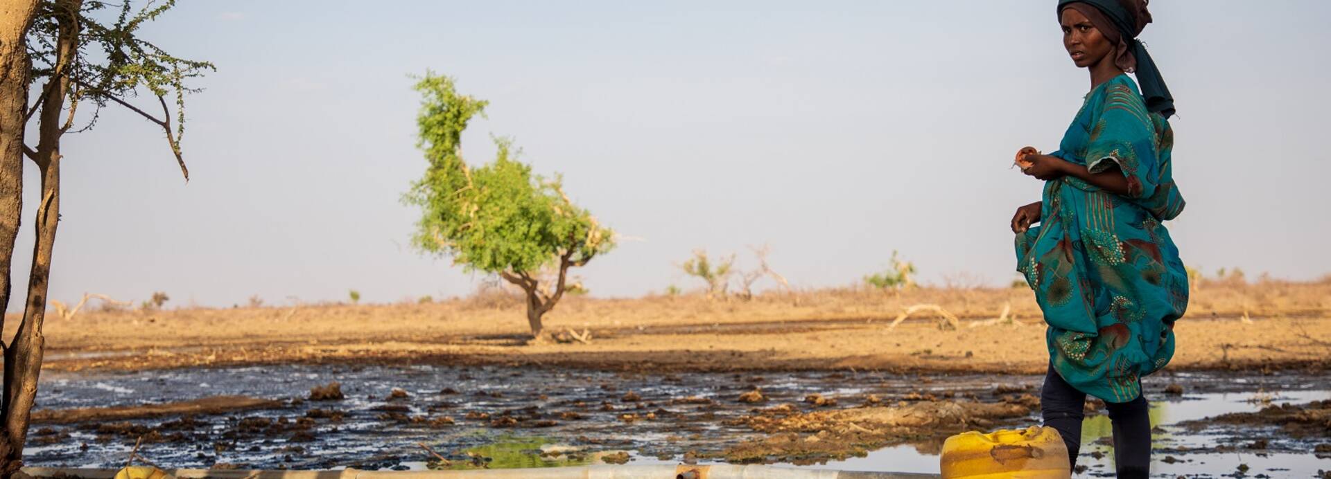 Eine Frau steht in einer trockenen Landschaft in Kenia. Eine Frau steht in einer trockenen Landschaft in Kenia am Rande eines Wasserlochs.