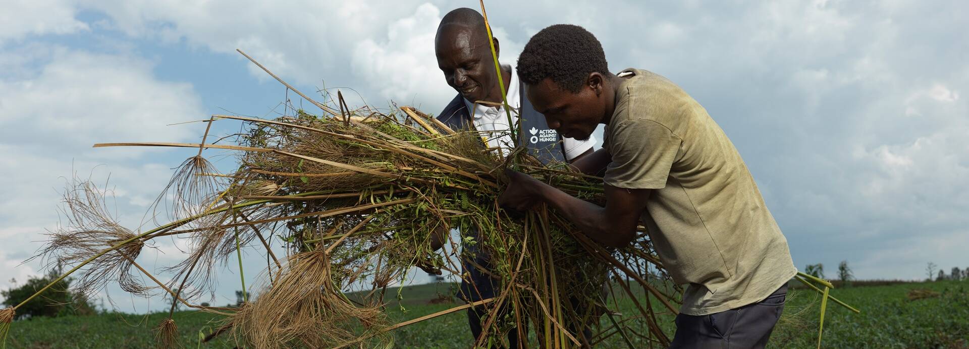 Ein Mitarbeiter von Aktion gegen den Hunger und ein Programmteilnehmer aus Uganda bedecken Ackerboden mit Mulch. Ein Mitarbeiter von Aktion gegen den Hunger und ein Programmteilnehmer aus Uganda bedecken Ackerboden mit Mulch.