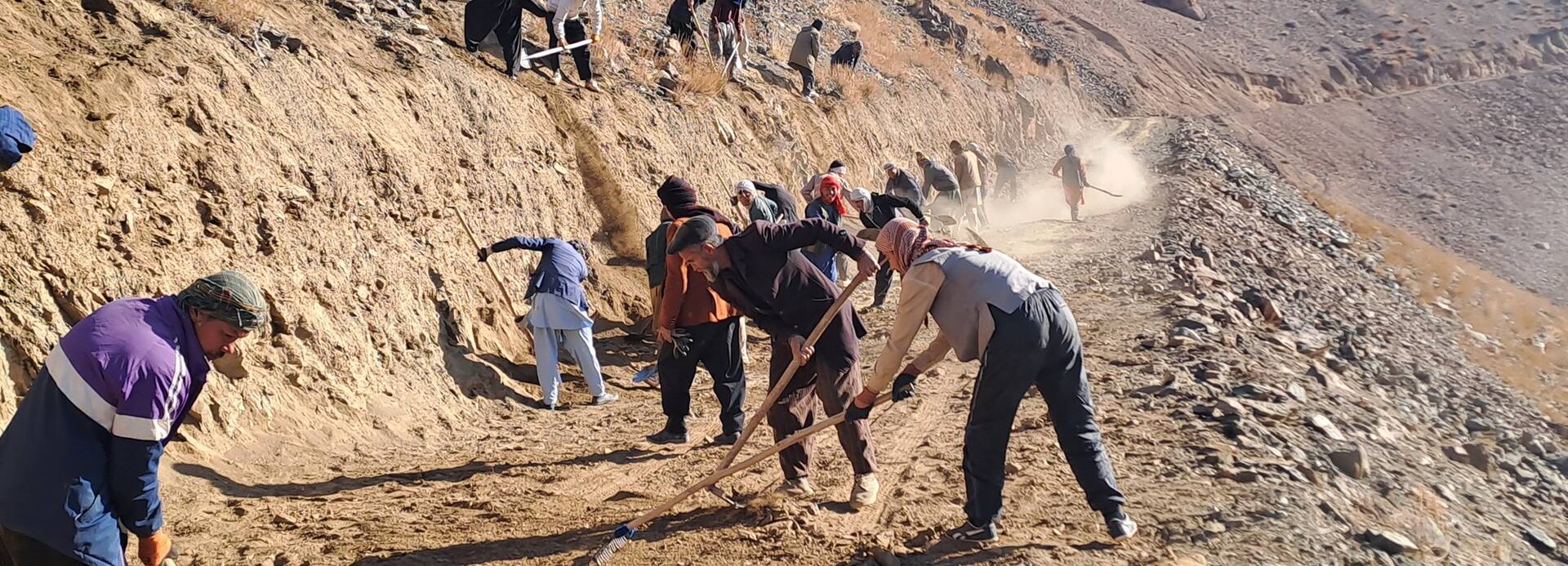 Stärkung der Widerstandsfähigkeit afghanischer Gemeinschaften durch verbesserte Lebensgrundlagen, Katastrophenrisikomanagement mit integrierter Ernährungssicherheit, psychischer Gesundheit und psychosozialer Unterstützung und WASH Unsere lokalen Teams in Afghanistan arbeiten mit Schaufeln und Rechen an der Befestigung einer Straße, die durch das Hochland von Daykundi führt.