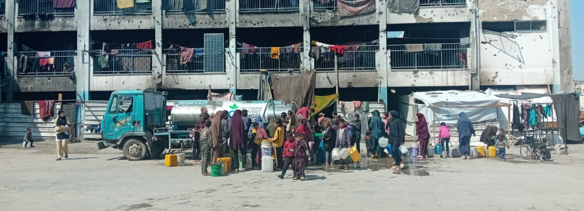 Menschen in Gaza stehen vor einem beschädigten Gebäude für Trinkwasser an. Menschen in Gaza stehen vor einem beschädigten Gebäude für Trinkwasser an.
