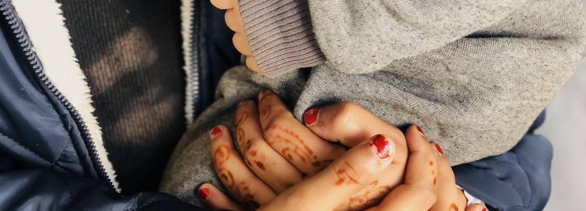 Aliya hält schützend die Hände um ihren Sohn. Eine Mutter hält schützend ihre Hände um ihr Kind.