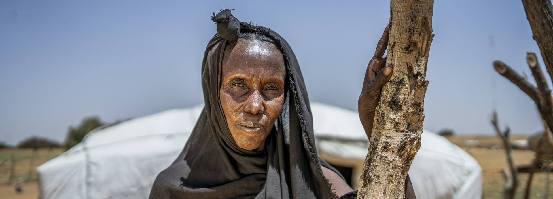 Eine Person steht vor einem Zelt in der trockenen Landschaft der Region Gao, Zentralmali, umgeben von den Spuren von Dürre und kargen Lebensbedingungen