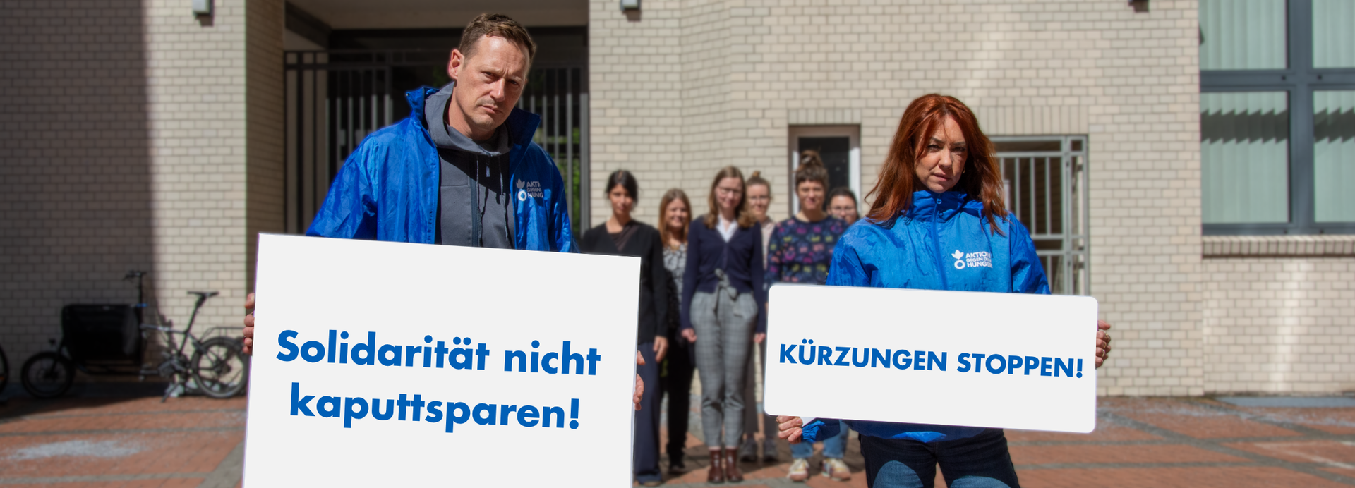 Mitarbeiter*innen von Aktion gegen den Hunger mit Protestschildern "Solidarität nicht kaputtsparen!" und "Kürzungen stoppen"