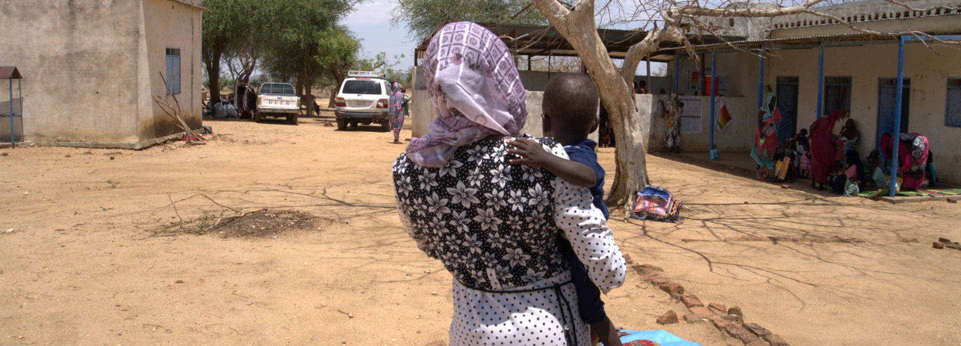 Mutter mit Kind in der Rückansicht. Die Fraz erhält in einer mobilen Klinik im Sudan therapeutische Spezialnahrung (RUTF) und Medikamente für ihr Kind. Mutter mit Kind in der Rückansicht. Die Fraz erhält in einer mobilen Klinik im Sudan therapeutische Spezialnahrung (RUTF) und Medikamente für ihr Kind.