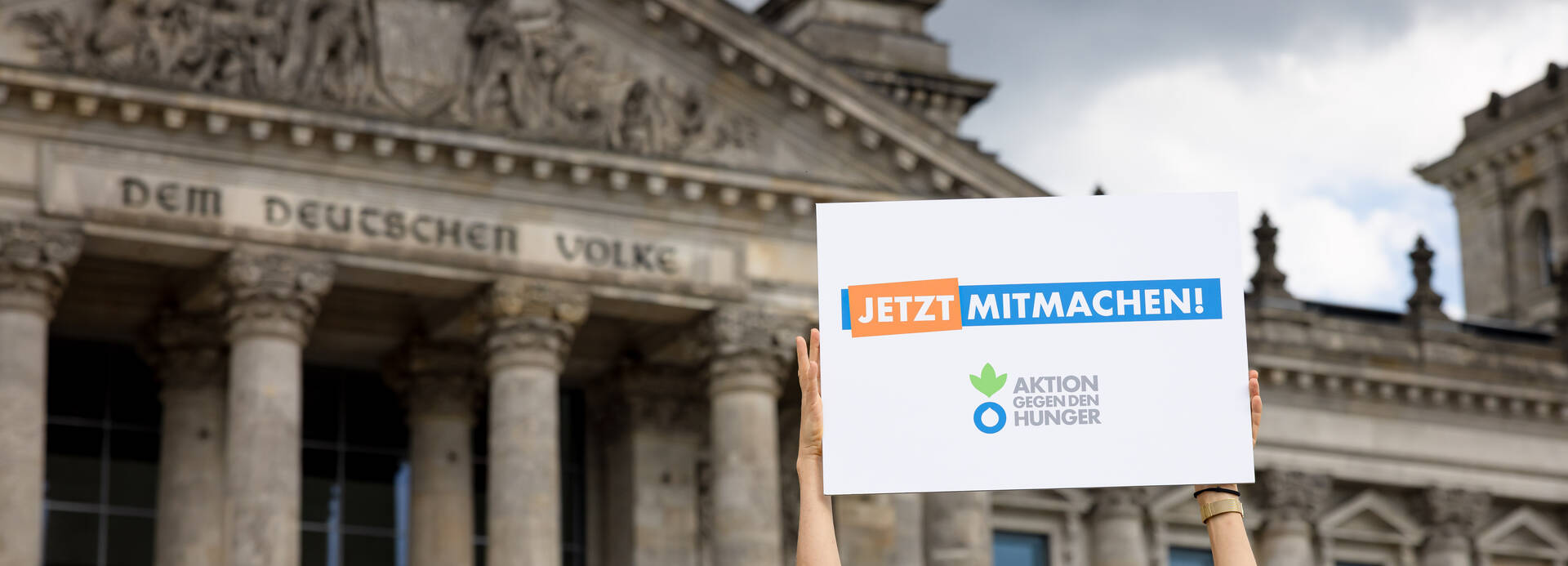 Frau hält Schild mit Aufschrift "Jetzt mitmachen" vor Bundestag
