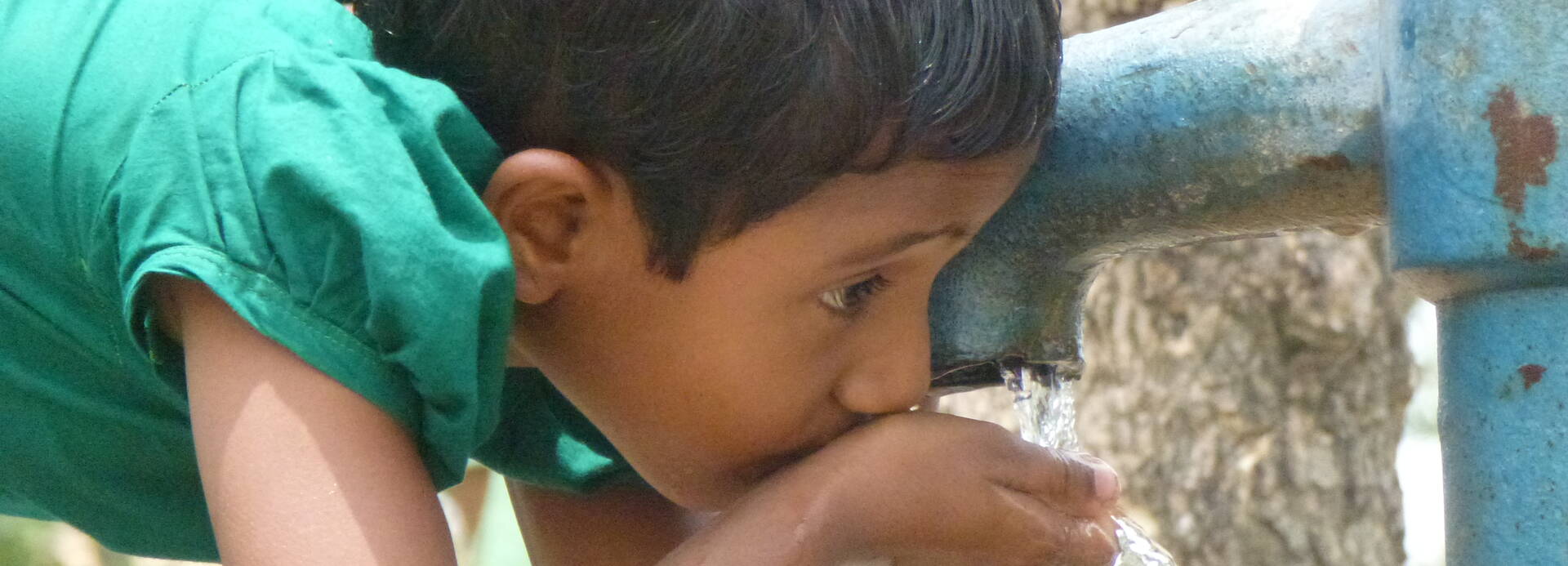 Kind trinkt Wasser aus einem Brunnen.