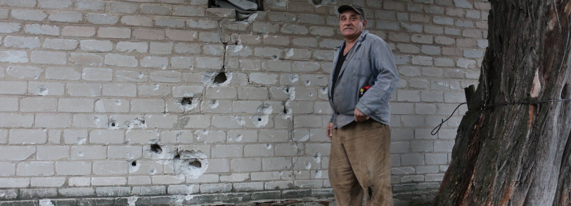 Ein Hilfeempfänger in der Ukraine steht vor einer zerschossenen Wand.