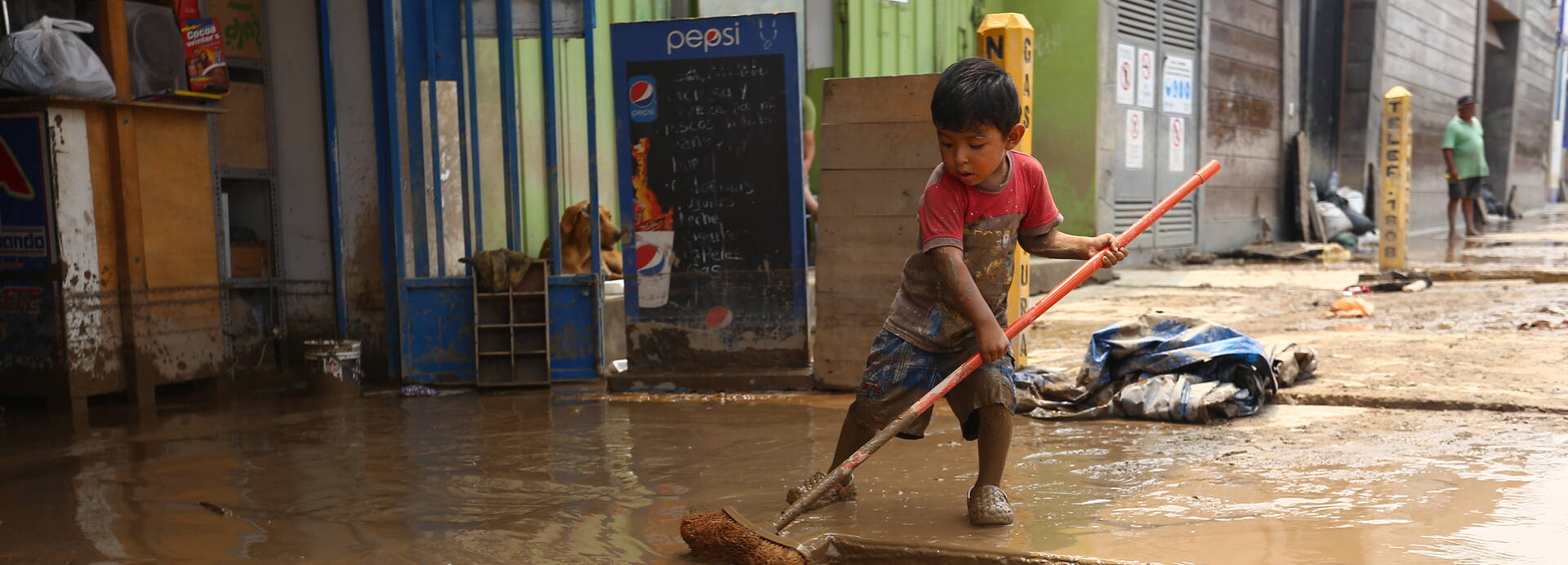 Kind fegt Wasser weg, nach starken Regenfällen in Peru