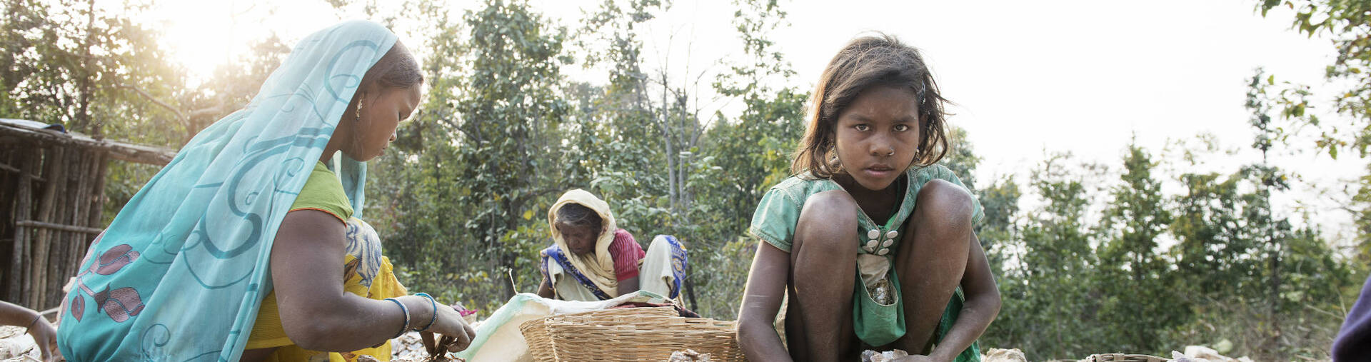 Kinderarbeit in Indien: Drei Kinder sitzen zwischen Steinen und Körben, um das Mineral Mica zu sortieren.