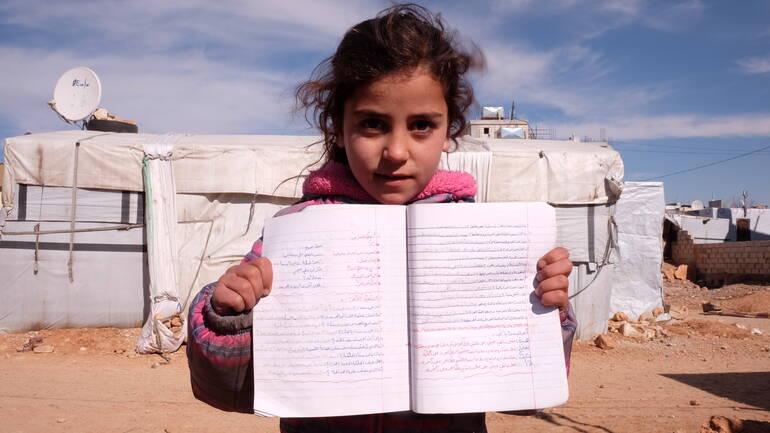 Mädchen in Syrien steht mit ihren Notizbuch vor der Kamera.