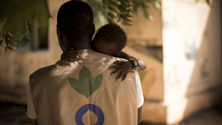 Mitarbeiter von Aktion gegen den Hunger hat kleines Kind auf dem Arm