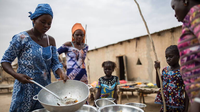 Frauen bereiten mit Kindern Essen vor.