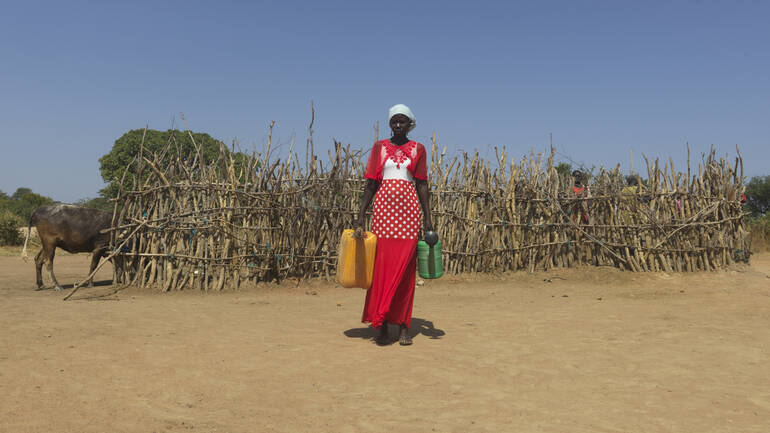 Frau aus dem Südsudan trägt Kanister mit Wasser