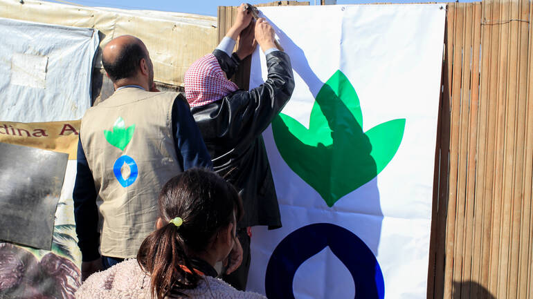 Mitarbeitende von Aktion gegen den Hunger hängen Plakat mit Logo auf