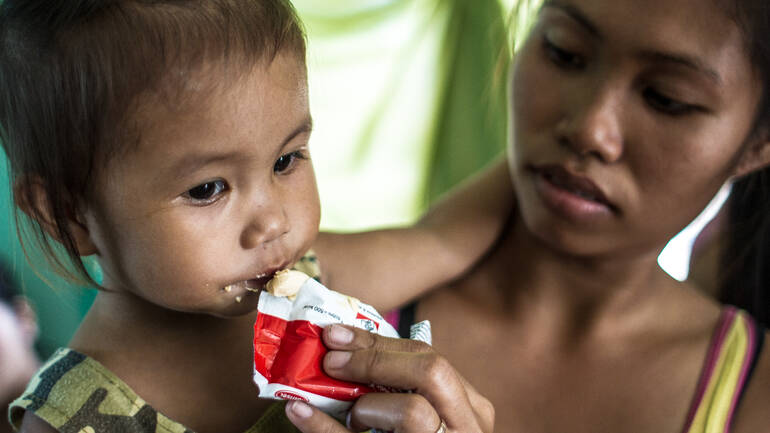 Mutter füttert Kind mit Plumpy Nut auf den Philippinen