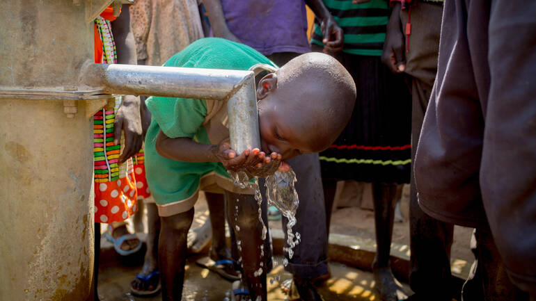 Kind aus dem Südsudan trinkt aus Brunnen