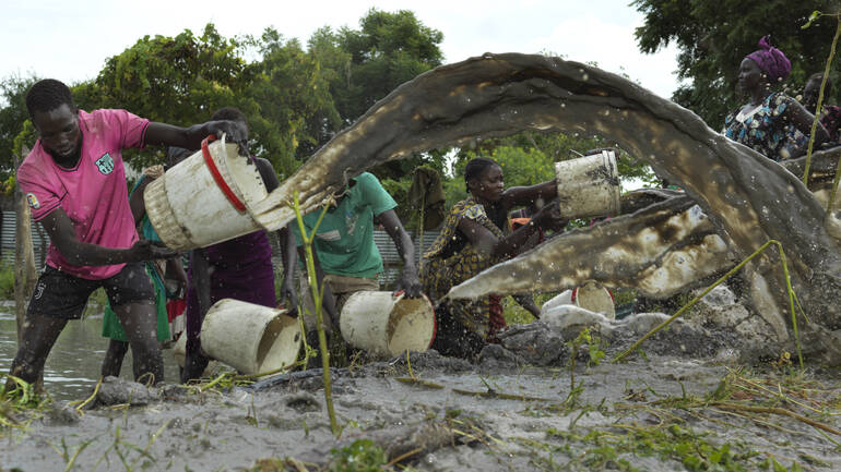 Die Bewohner*innen einer Gemeinde im Südsudan versuchen, ihr Dorf mithilfe von Eimern vom Flutwasser zu befreien