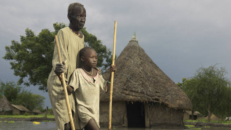 Mutter und Kind kämpfen sich mit Stöcken durch die Fluten im Südsudan